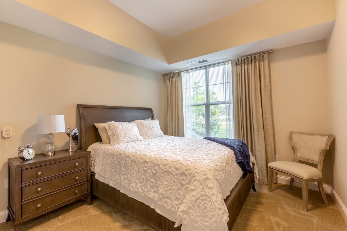 A cozy bedroom featuring a neatly made bed with white linens and a large window with curtains.