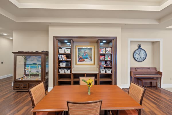A conference room featuring a wooden table, surrounded by chairs, with bookshelves and artwork in the background.