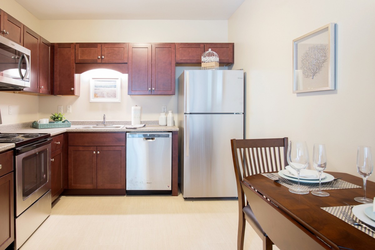 A modern kitchen with stainless steel appliances and wooden dining furniture.