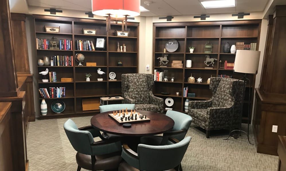 A cozy library corner featuring bookshelves, a chess set on a round table, and comfortable seating.