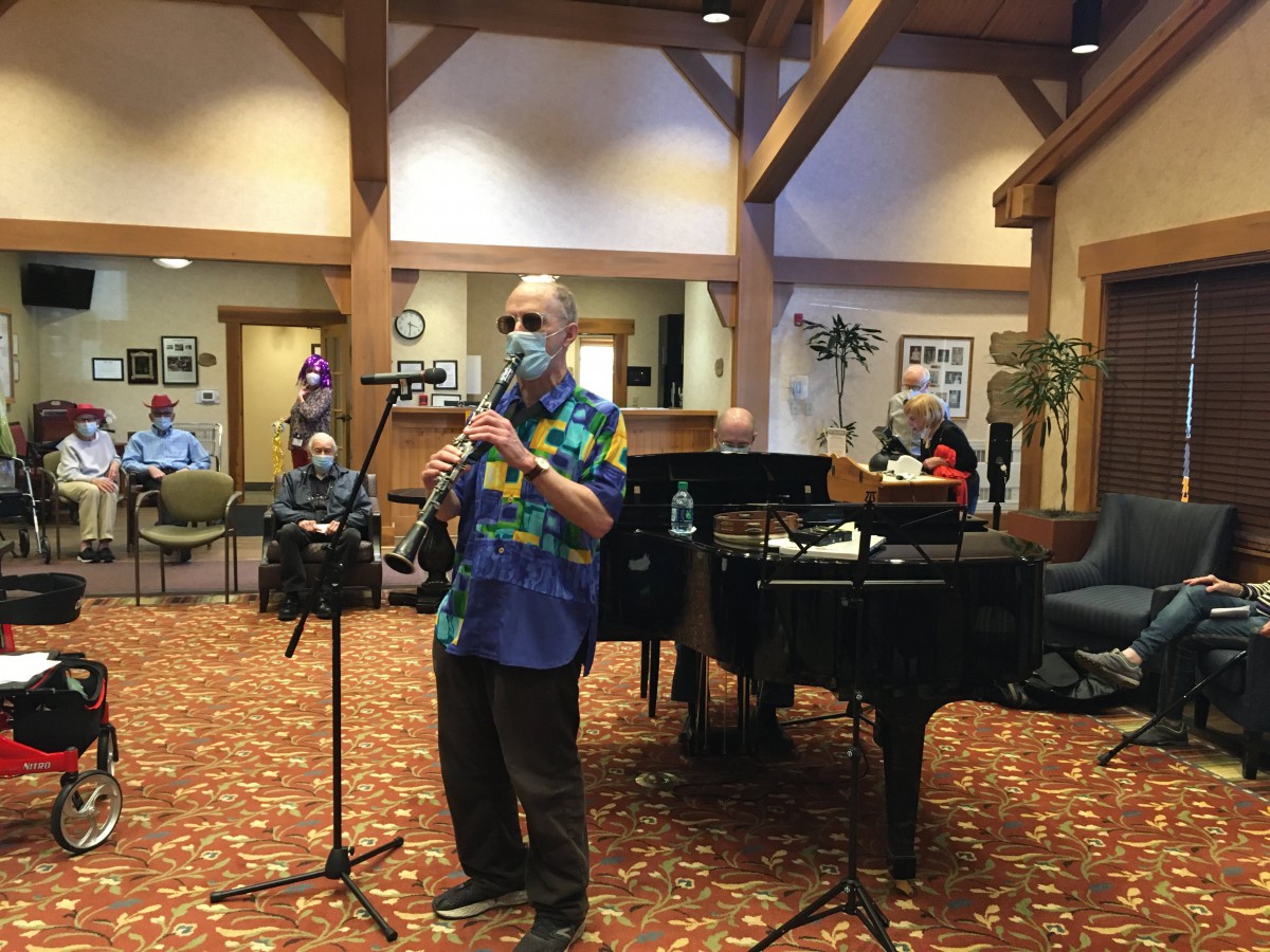 A musician performs on the clarinet in front of a grand piano, entertaining an audience indoors.