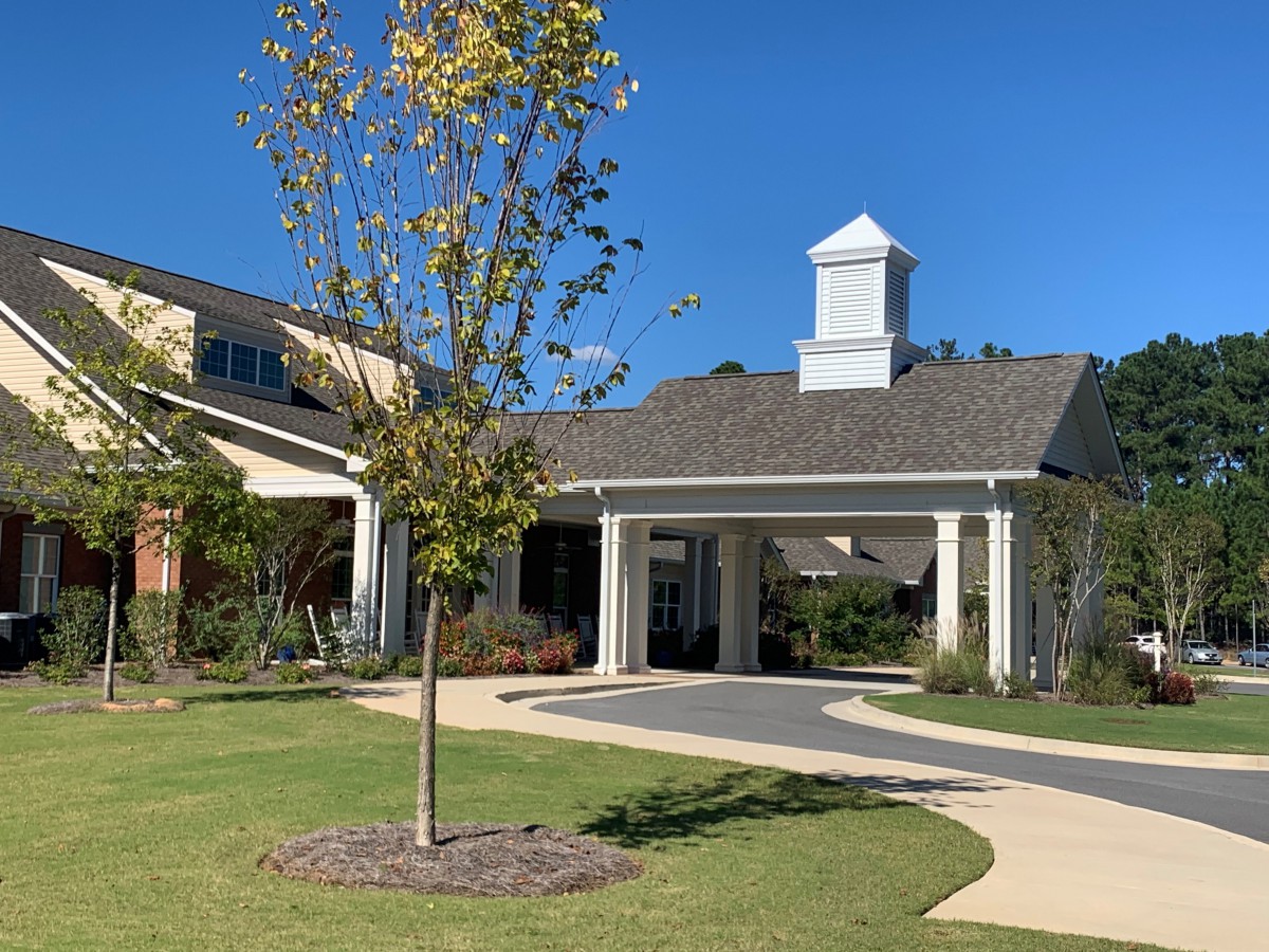 A modern building entrance with a covered driveway, lush landscaping, and a clear blue sky.