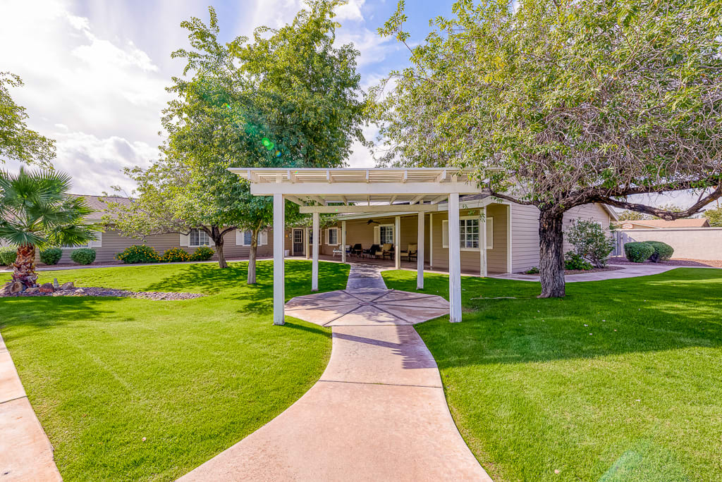 A serene garden pathway leading to a pergola, surrounded by lush greenery and trees.
