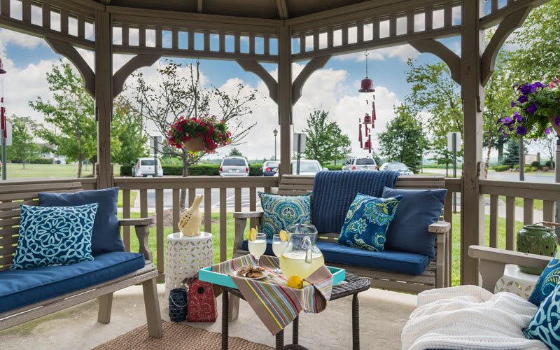 A cozy gazebo with blue-cushioned seating and a table set for refreshments, perfect for outdoor relaxation.