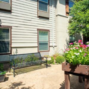 A peaceful garden area with a bench and colorful flowers in front of a building.