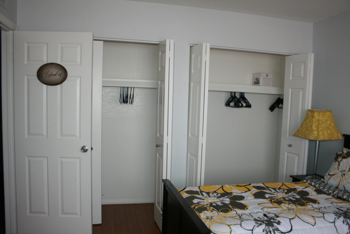 A bedroom with open closet doors, displaying a few hangers and a colorful bedspread on the bed.