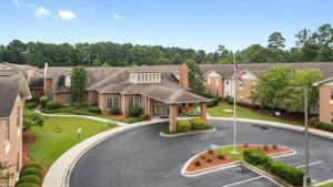 A brick building with a driveway and flagpole, surrounded by trees and landscaping.