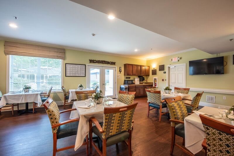 A cozy dining room with multiple tables and chairs, featuring a small kitchen area.