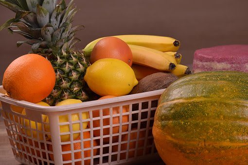 A basket filled with a variety of fresh fruits including pineapple, bananas, melon, oranges, lemons, and kiwi.