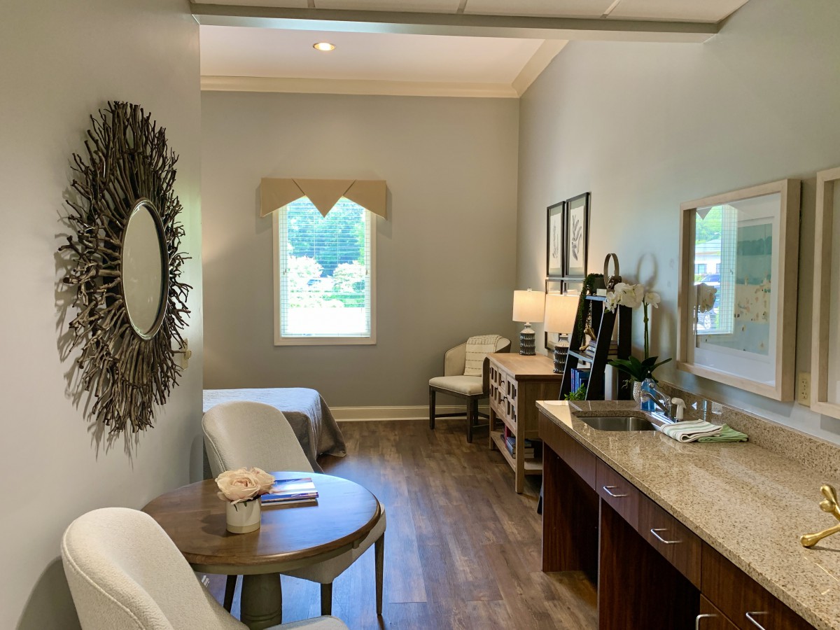 A modern and minimalist bedroom with wooden flooring, featuring a circular mirror, elegant furniture, and soft lighting.