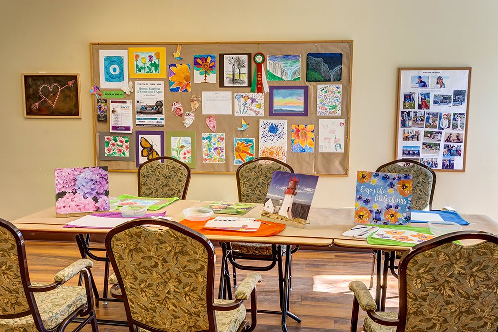 An art room with tables and chairs, showcasing colorful artwork on a bulletin board.