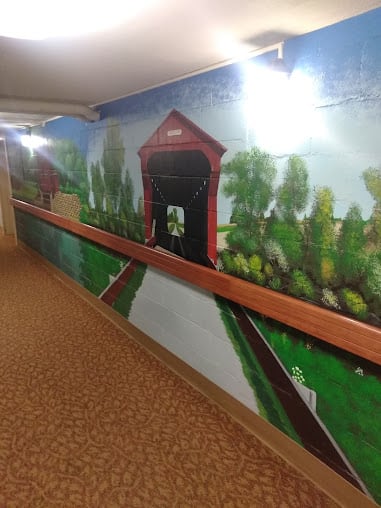 A hallway mural depicting a scenic landscape with a covered bridge.