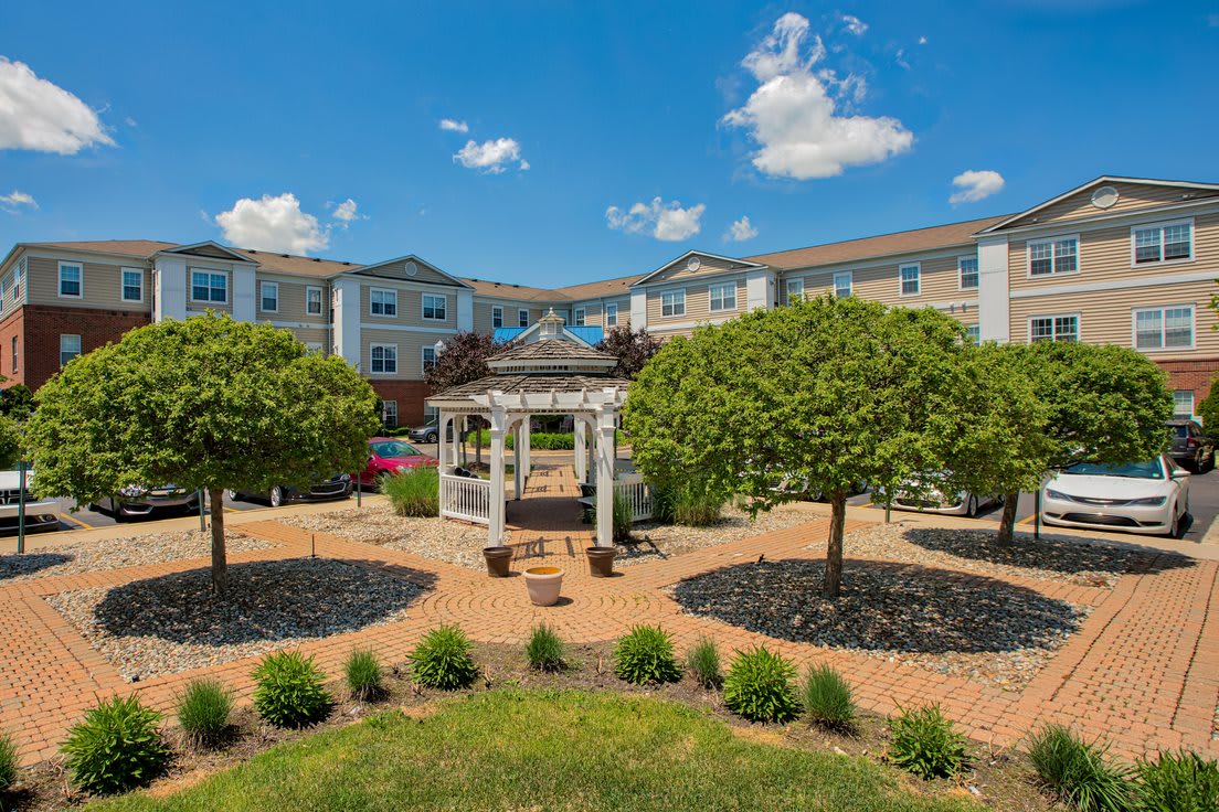 A beautifully landscaped garden with a gazebo in front of a residential building on a sunny day.
