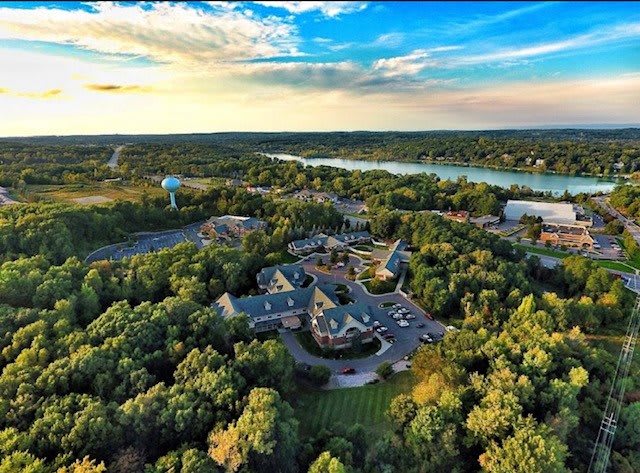 A scenic aerial view of a landscape featuring a river, lush forest, and buildings under a vibrant sunset sky.