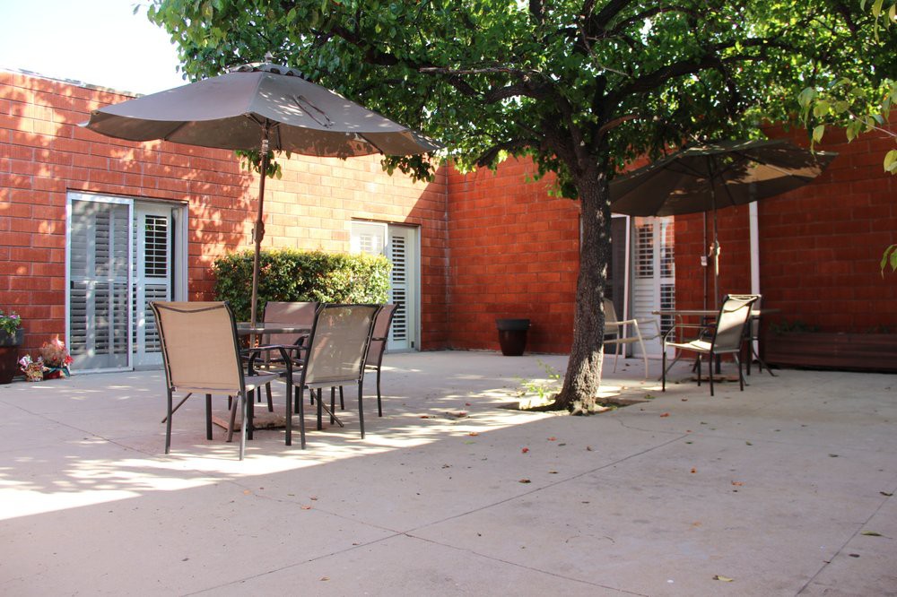 A sunny patio with outdoor furniture and umbrellas next to a brick wall.