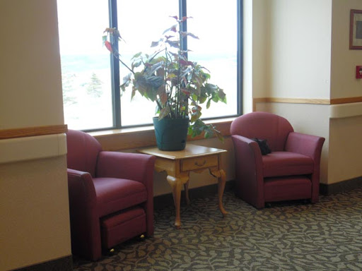 A cozy waiting area featuring two red chairs, a small table, and an indoor plant by the window.