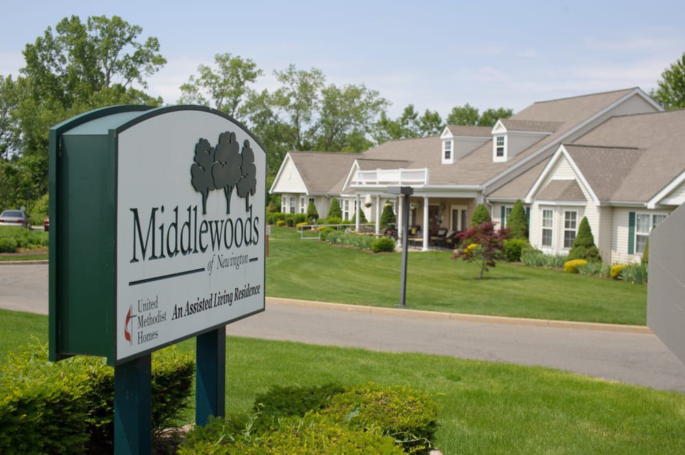 A view of Middlewoods assisted living community with a sign in the foreground and residential buildings in the background.