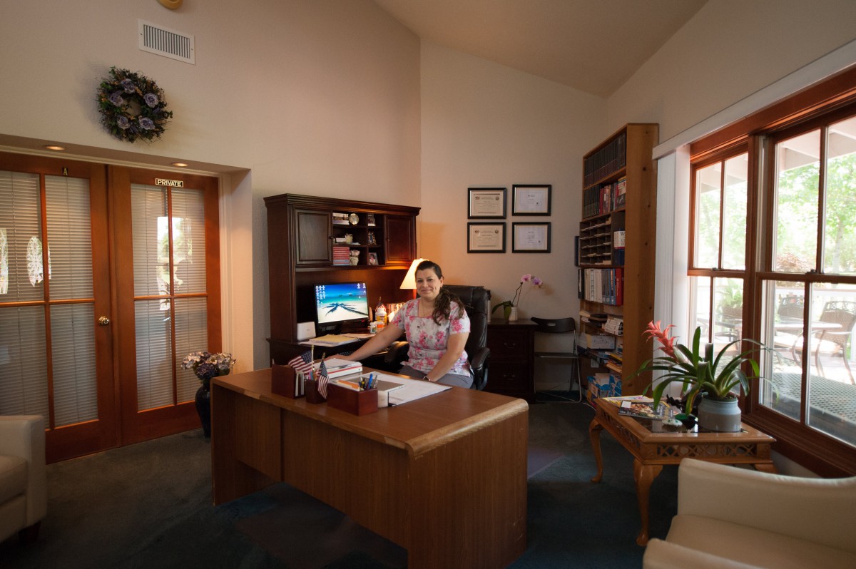 A person sits at a desk in a well-organized office space with a computer and bookshelves.