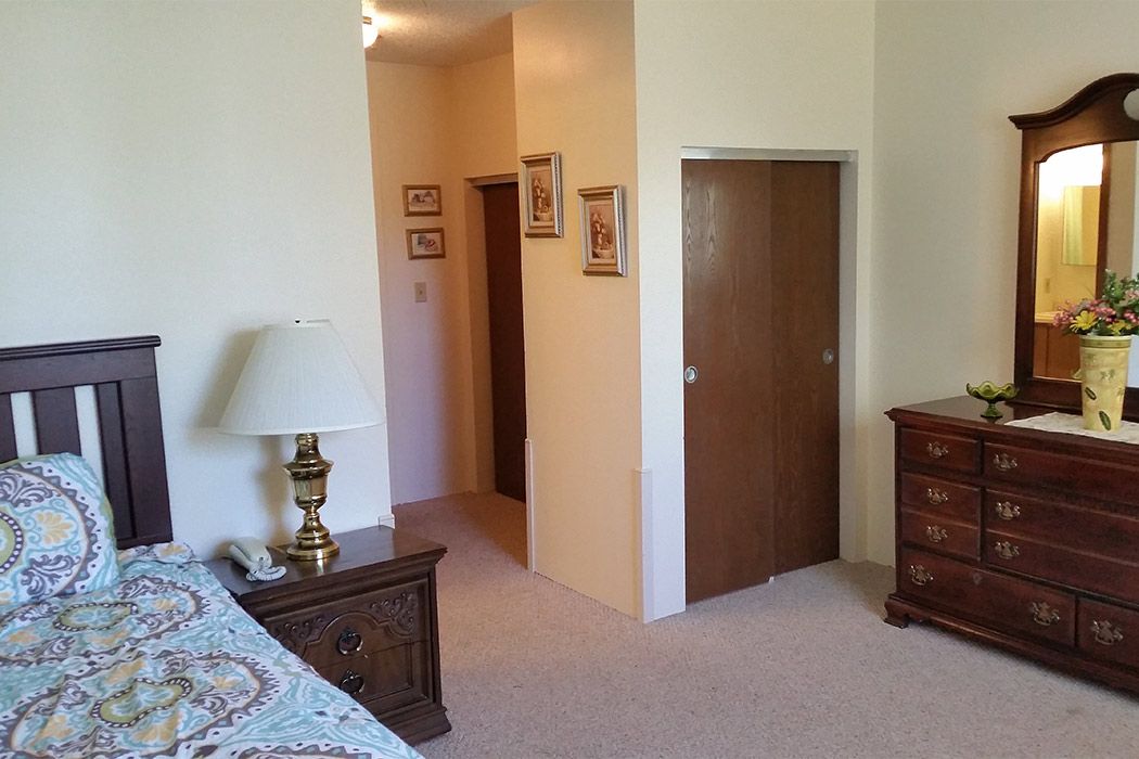A cozy bedroom with a lamp on a nightstand, a dresser, and artwork on the walls.