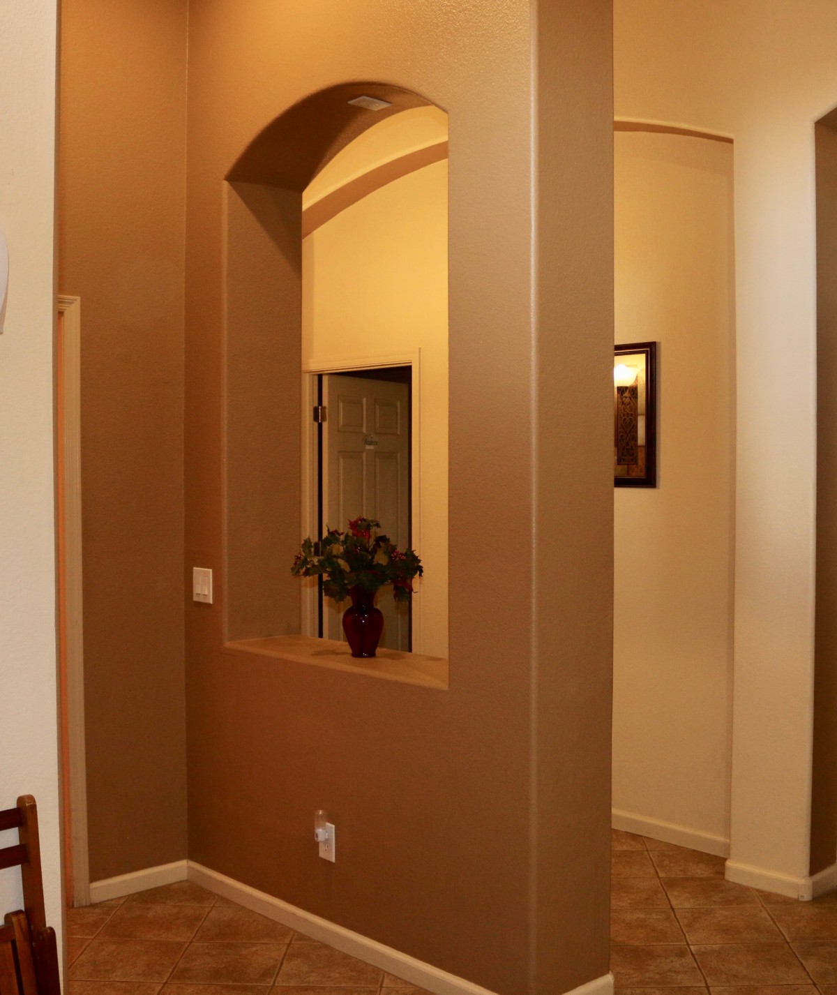 A warmly lit hallway with an archway and decorative plant in a vase.