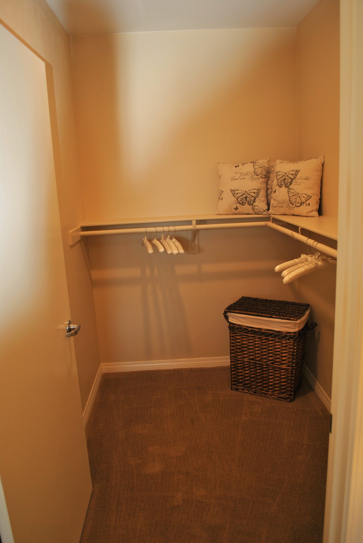 An empty walk-in closet with a few hangers, a basket, and decorative pillows.