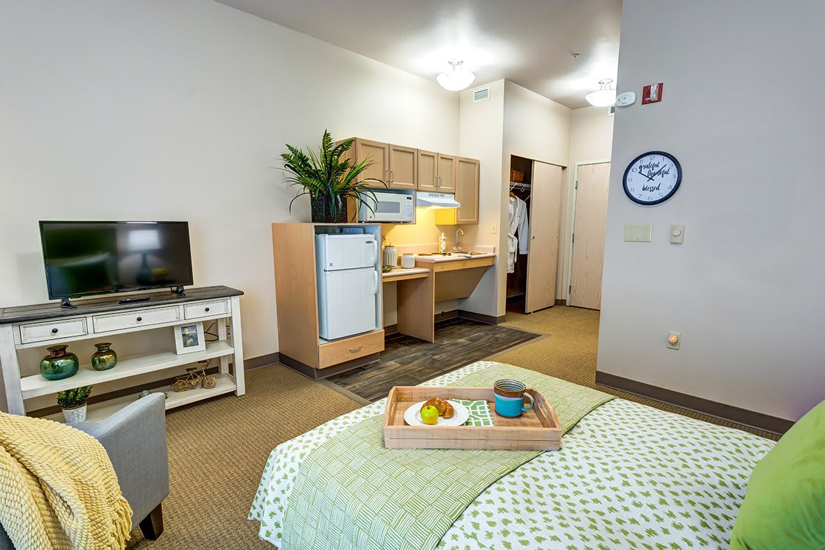 A cozy studio apartment with a kitchenette, featuring a bed, TV, and small dining area.