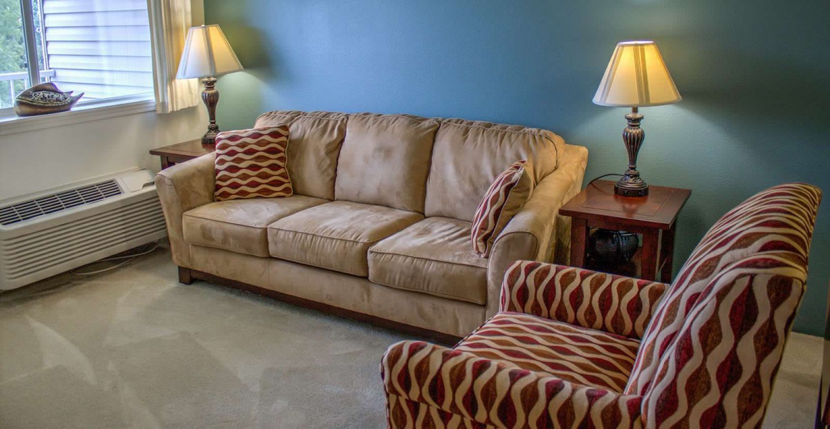 A cozy living room setup with a beige sofa, patterned armchair, and warm lighting.