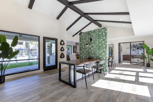 A modern dining area featuring a green accent wall and wooden beams, flooded with natural light.