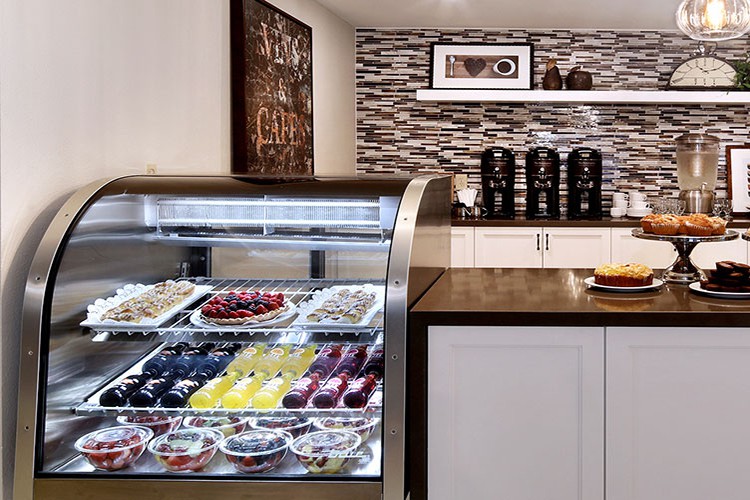 A cozy cafe with a dessert display case filled with pastries and a coffee station in the background.