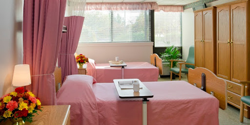 A bright and clean hospital patient room with two beds, each equipped with a bedside table.