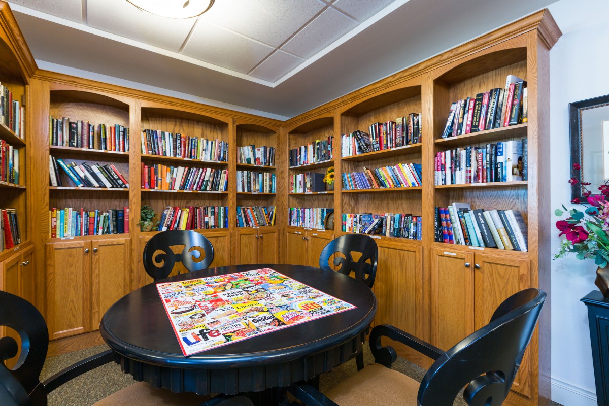 A cozy library corner with bookshelves, a round table, and a puzzle laid out.