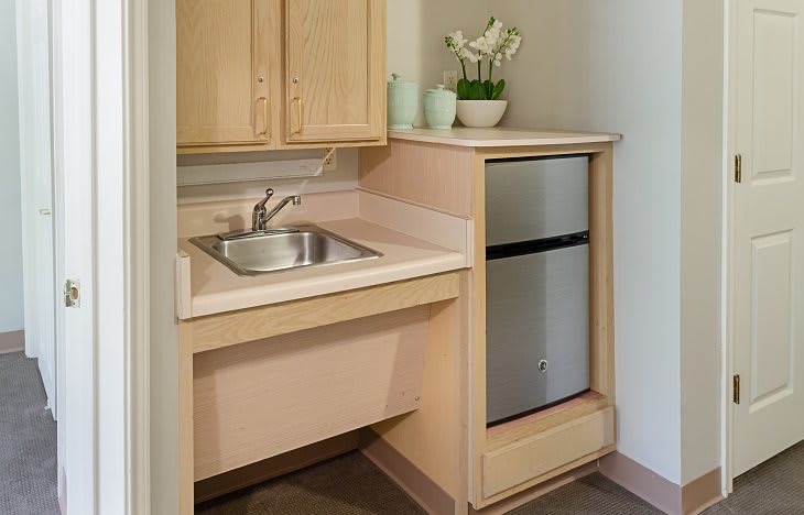 A compact kitchenette featuring a sink, a small fridge, and wooden cabinets.