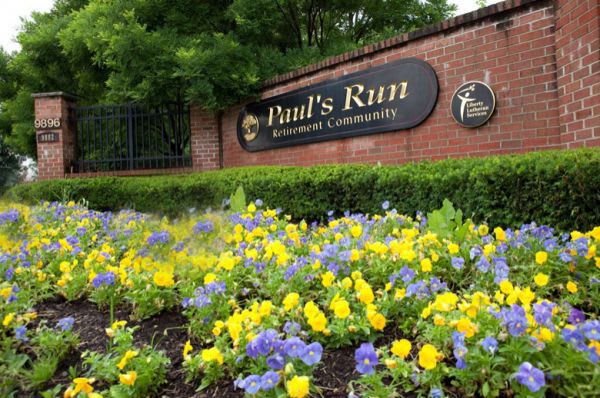 Entrance sign of a community surrounded by vibrant yellow and purple flowers.