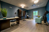 A modern office interior with wooden flooring, featuring a desk, chairs, and elegant lighting.
