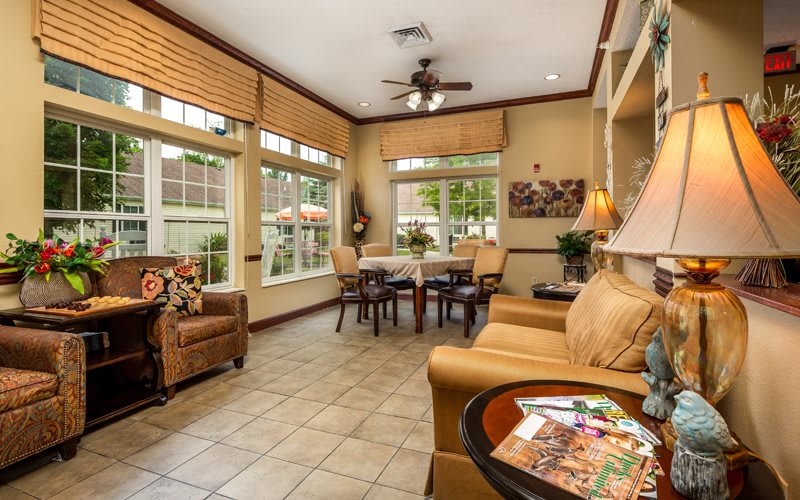A cozy living room with ample natural light, featuring comfortable seating and large windows.