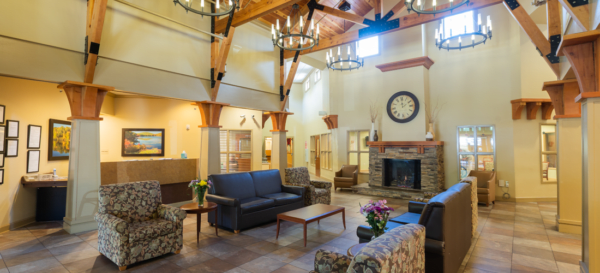 A cozy living room with comfortable seating, chandeliers, and a fireplace, featuring wood beam architecture and natural lighting.