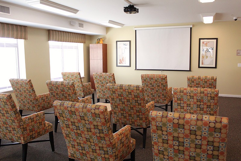A small conference room with patterned chairs facing a projector screen.