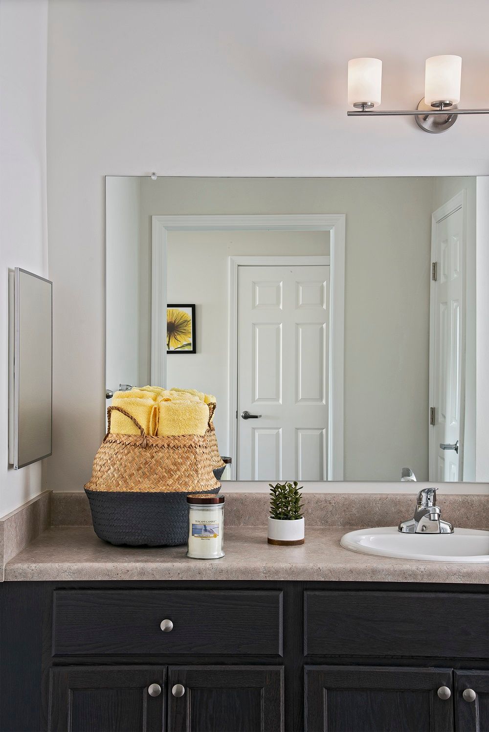 A neatly organized bathroom countertop with a mirror reflecting the door, featuring towels in a basket and small plant decor.
