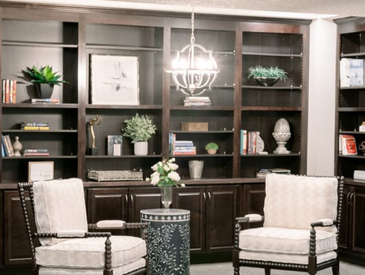 A cozy living room setting with a large bookshelf, two chairs, and decorative plants.