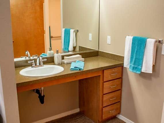 A clean and organized bathroom with a sink, mirror, and teal towels.