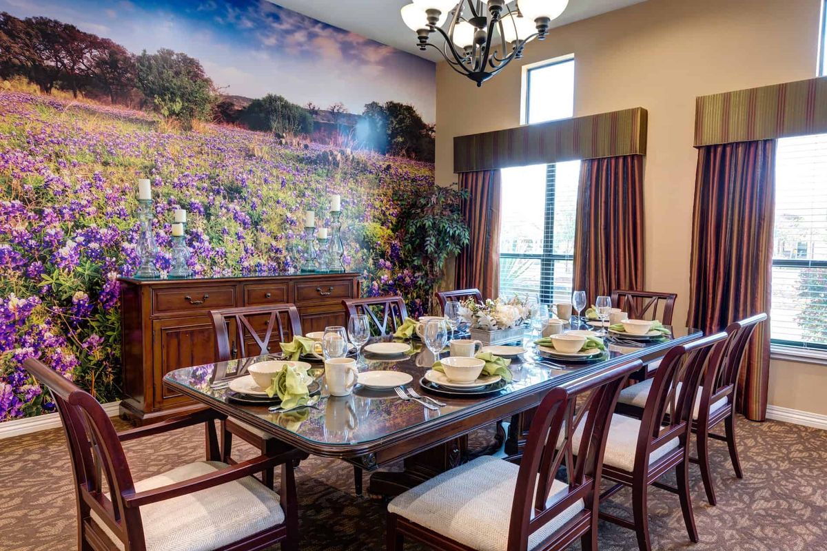 A well-decorated dining room featuring a table set for a meal, surrounded by chairs and illuminated by a chandelier, with a colorful wall mural in the background.