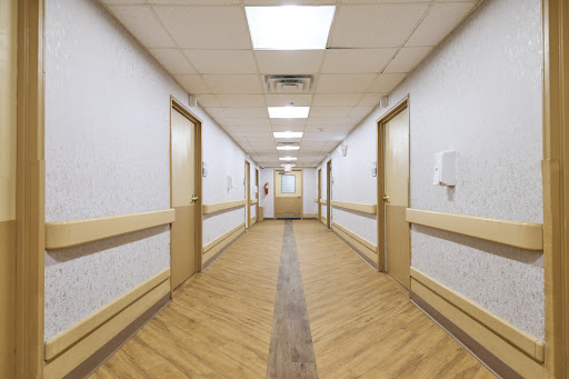 A well-lit hospital hallway featuring doors on either side and a wooden floor.