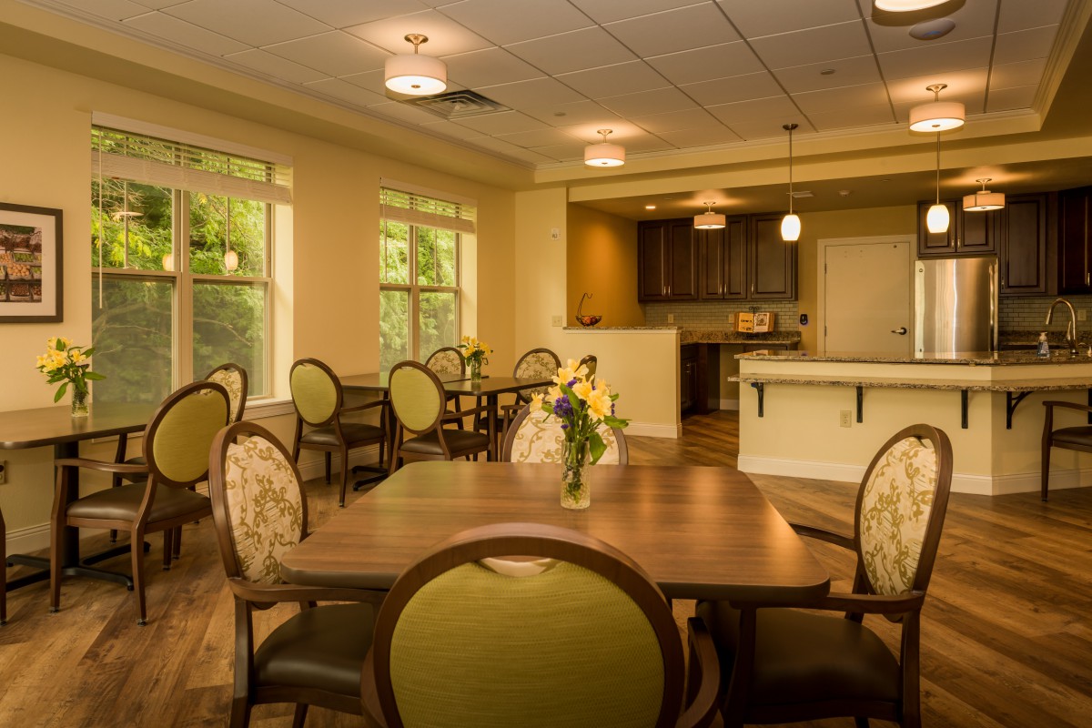 A cozy dining area featuring wooden tables and upholstered chairs, with natural lighting illuminating the space.