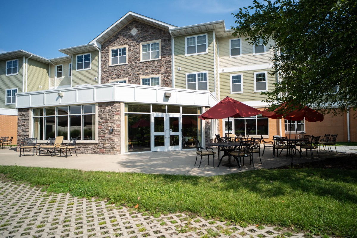 A modern building with outdoor seating including tables and umbrellas, surrounded by grass.