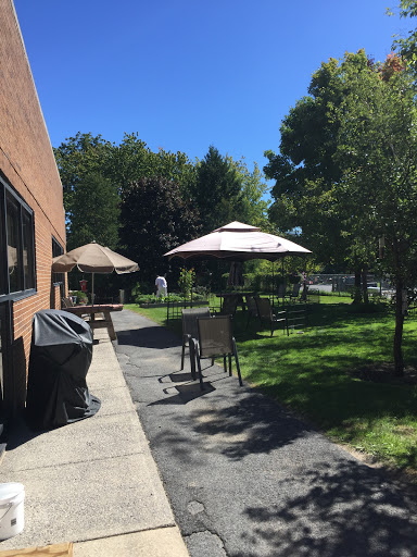 A sunny outdoor area featuring seating and shaded umbrellas, surrounded by greenery.
