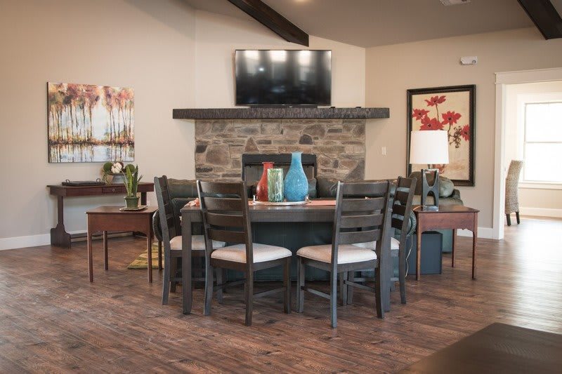A cozy dining room with a round table and chairs, set against a stone fireplace, decorated with colorful vases and modern artwork.
