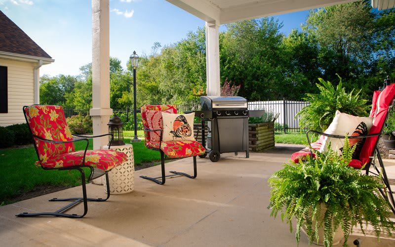 A cozy patio setup with chairs, a grill, and vibrant plants in a garden setting.