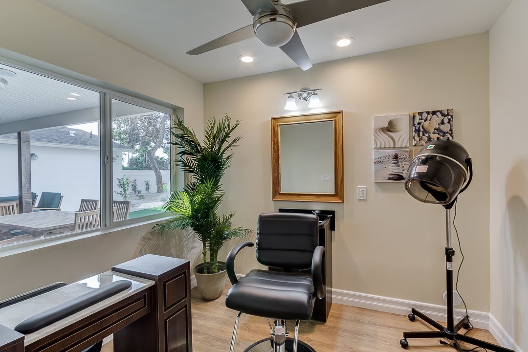 A modern hair salon interior with a chair facing a mirror, complemented by lush plants and ample natural lighting.