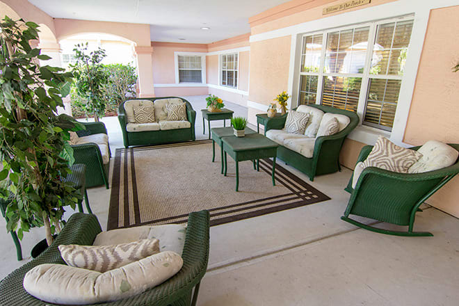 A cozy patio setup with wicker furniture and cushioned seating around a central rug, complemented by green plants.