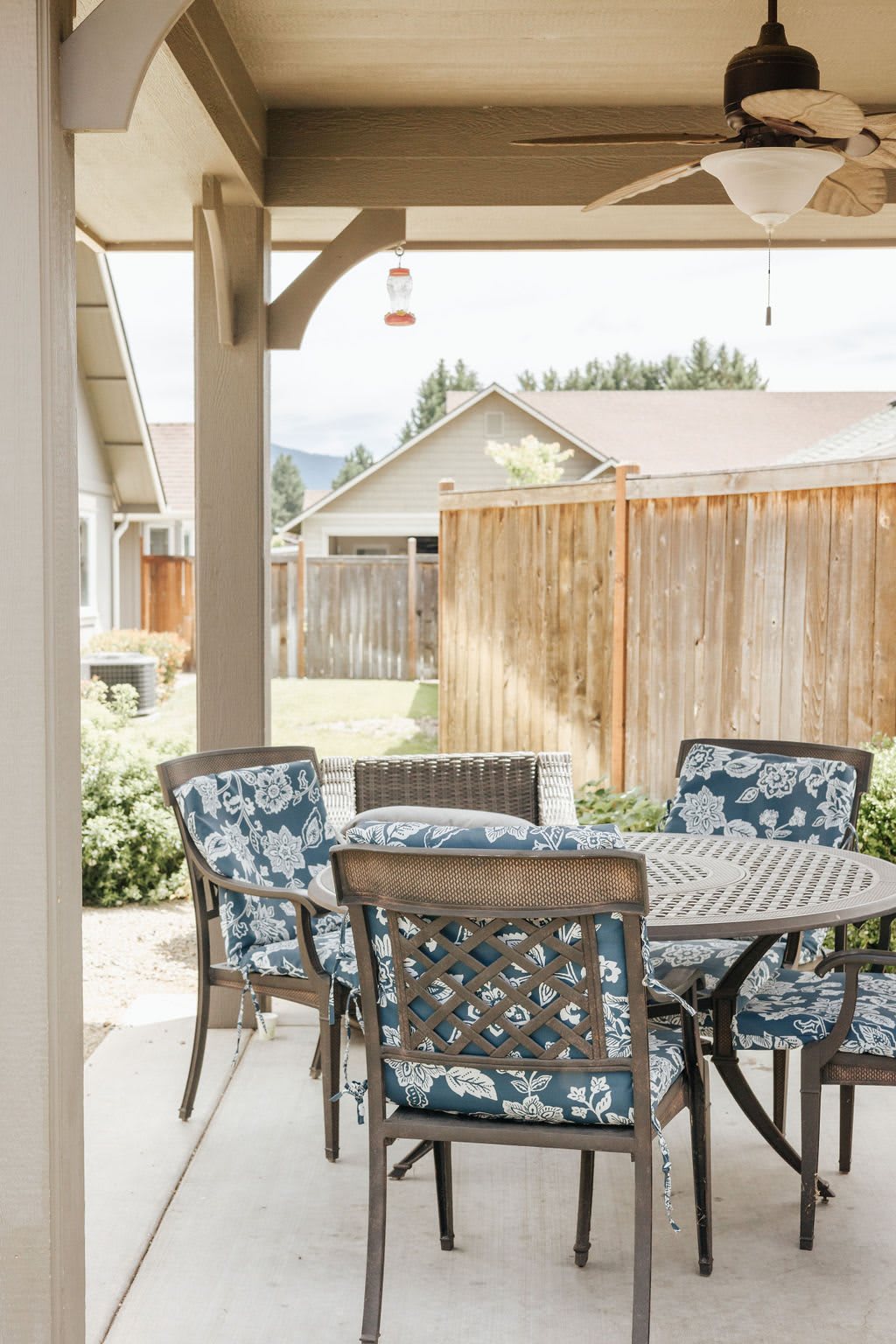 A cozy patio area with a round table and cushioned chairs, set against a wooden fence in a backyard.